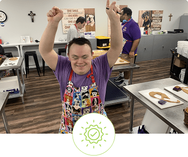 A joyful man raising his fists in celebration at an art table.